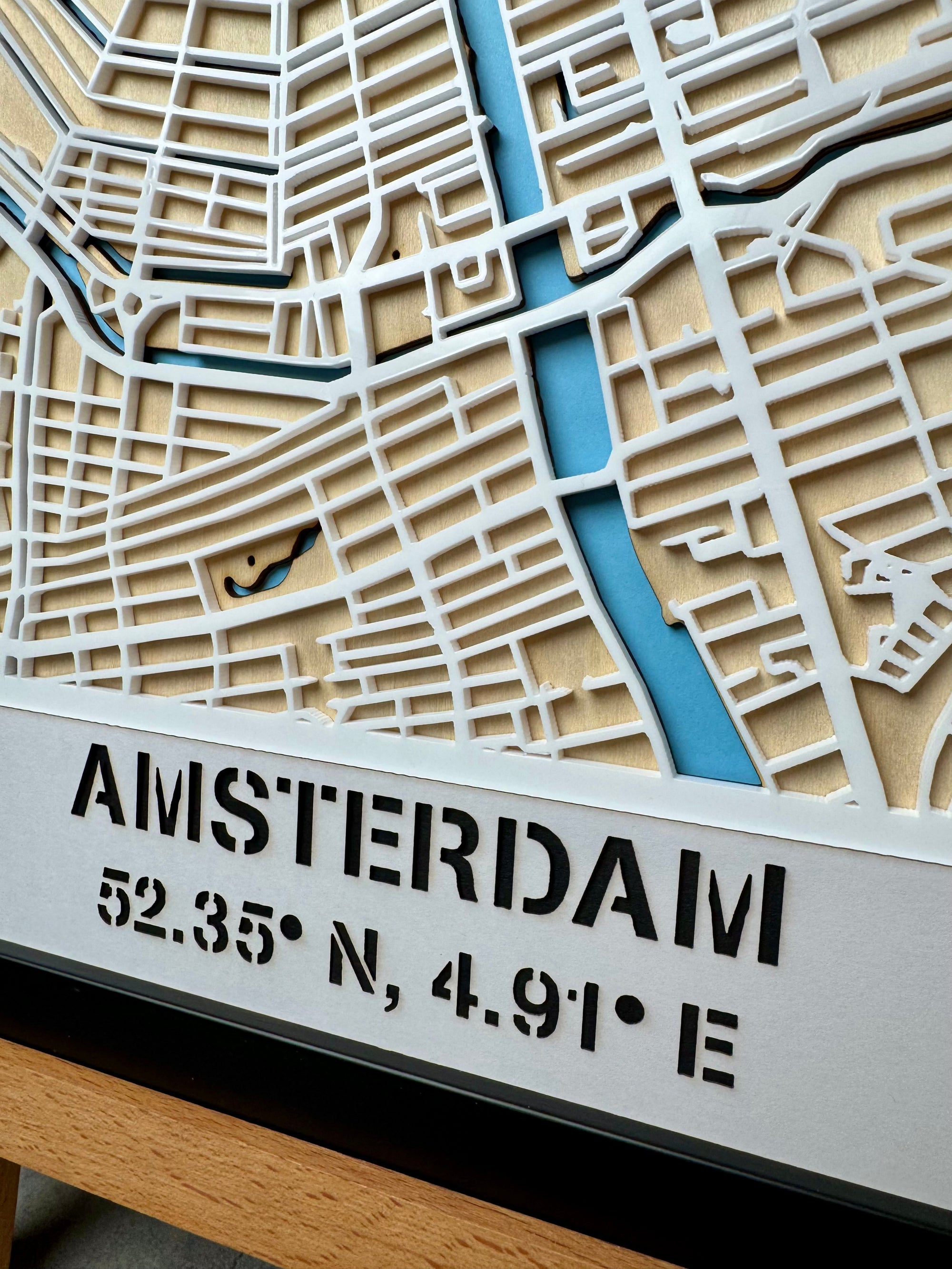 Close-up of Amsterdam city map wall art showing the “Amsterdam” title and geographic coordinates – detailed laser-cut wooden map artwork with blue canals and layered design for modern wall decor