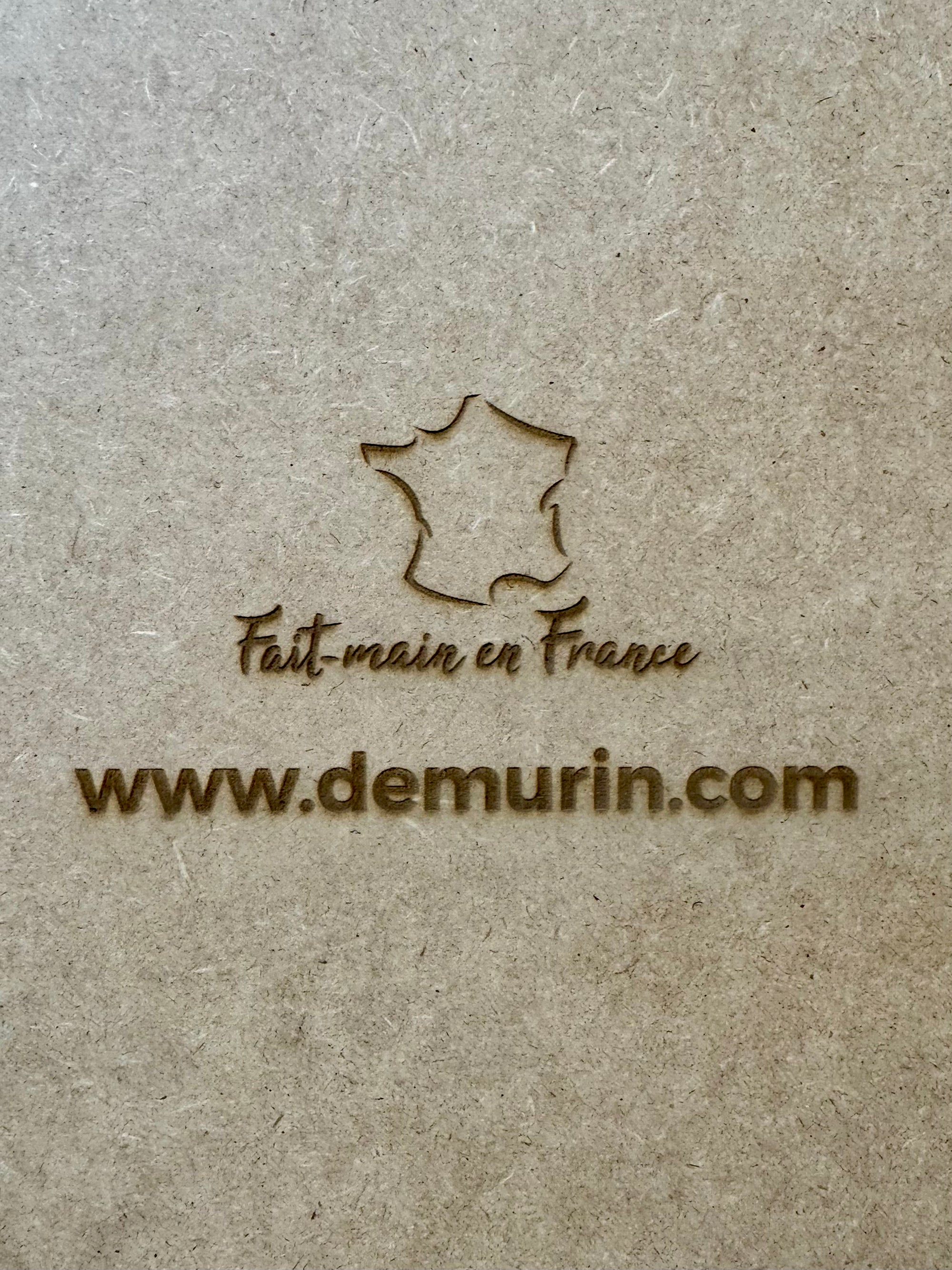Extreme close-up of laser engraving on natural oak wood showing “Fait main en France” and www.demurin.com on the back of a San Juan 3D city map frame, showcasing premium handcrafted quality.