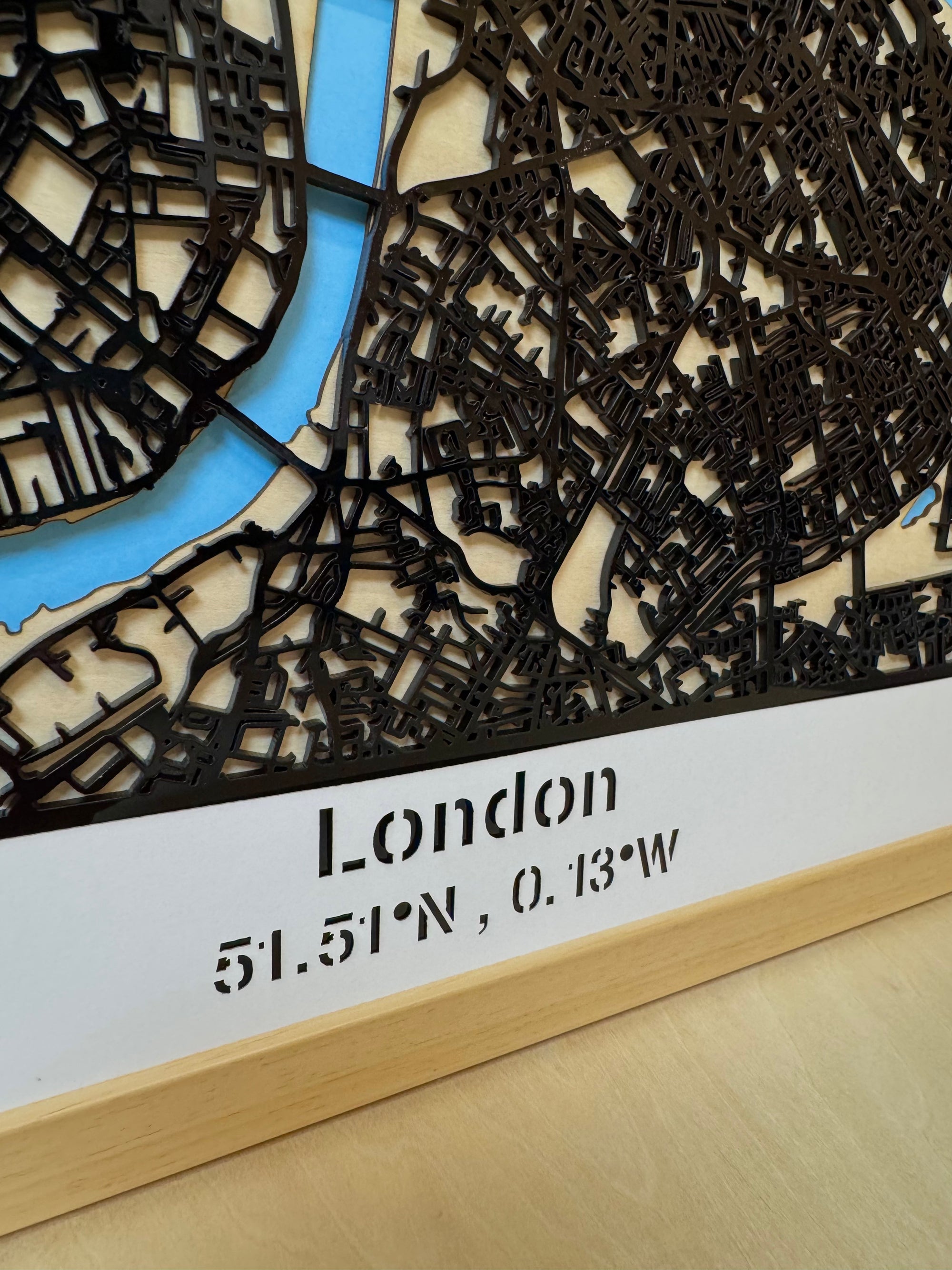 Detailed close-up of London city map wall decor with laser-engraved “London” title and precise latitude and longitude coordinates on natural oak wood frame – 3D layered street map handcrafted in France.